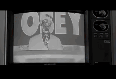 Gif du film « They live ». Une première scène avec l’acteur principal en couleur et ses lunettes qui regarde la télévision avec le présentateur et derrière ce-dernier &ldquo;Obey&rdquo;.